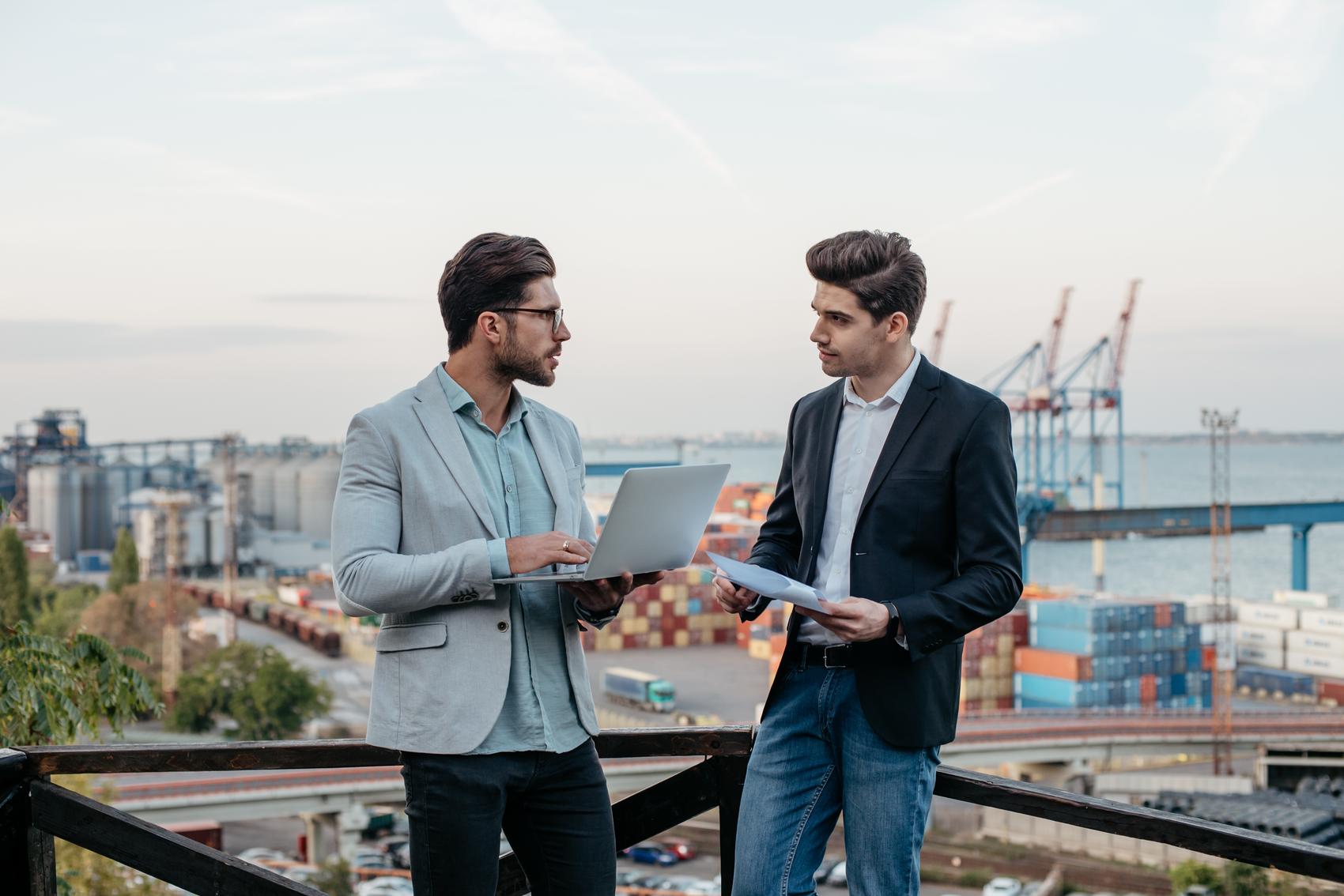 Een klant en een adviseur in gesprek met laptop en documenten bij de Rotterdamse haven, passend bij financieel advies in Rotterdam.
