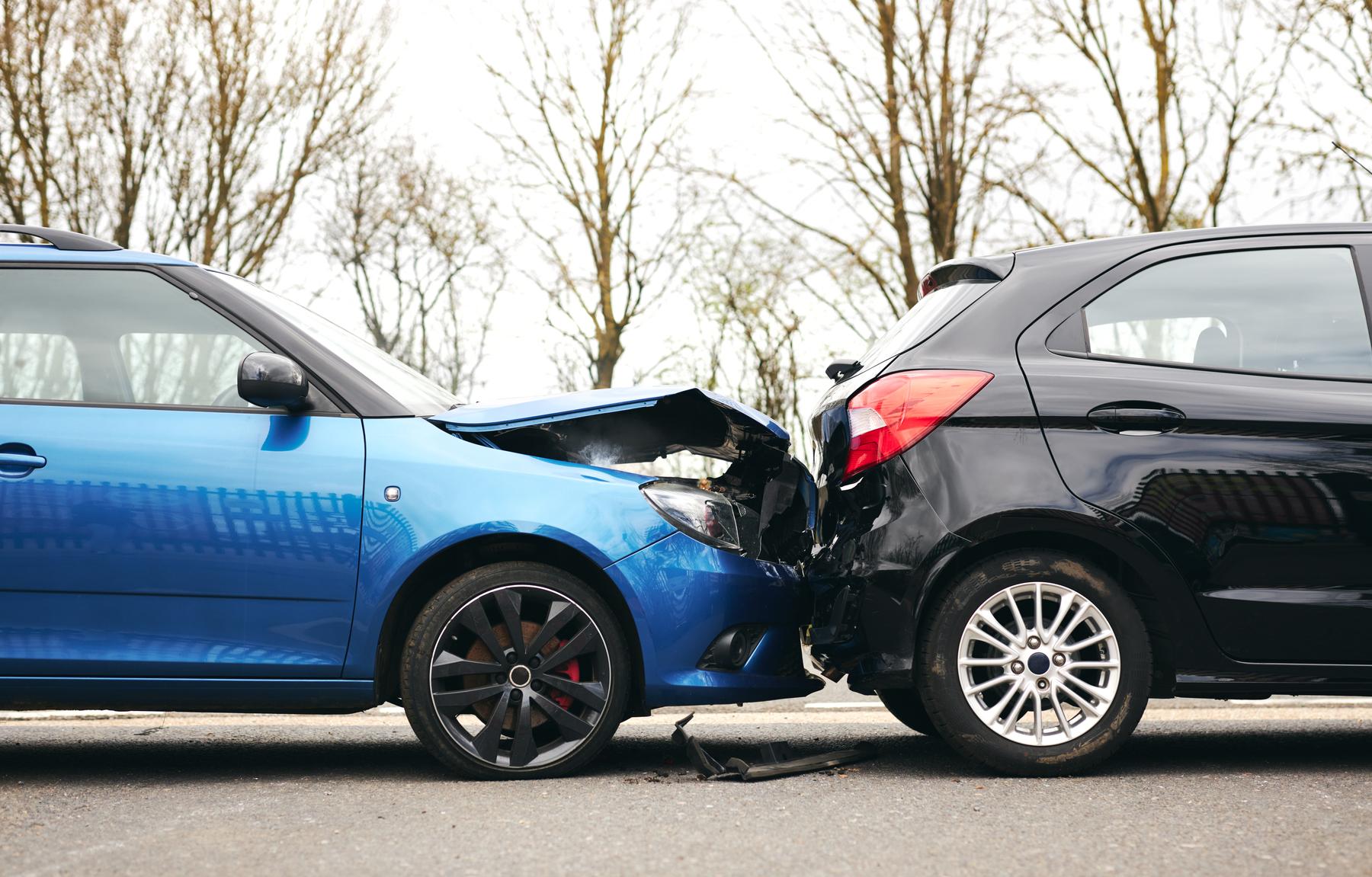 Kop-staartbotsing tussen een blauwe en een zwarte auto met zichtbare schade aan de voor- en achterkant, passend bij autoschade melden bij Van der Velden Adviseurs.