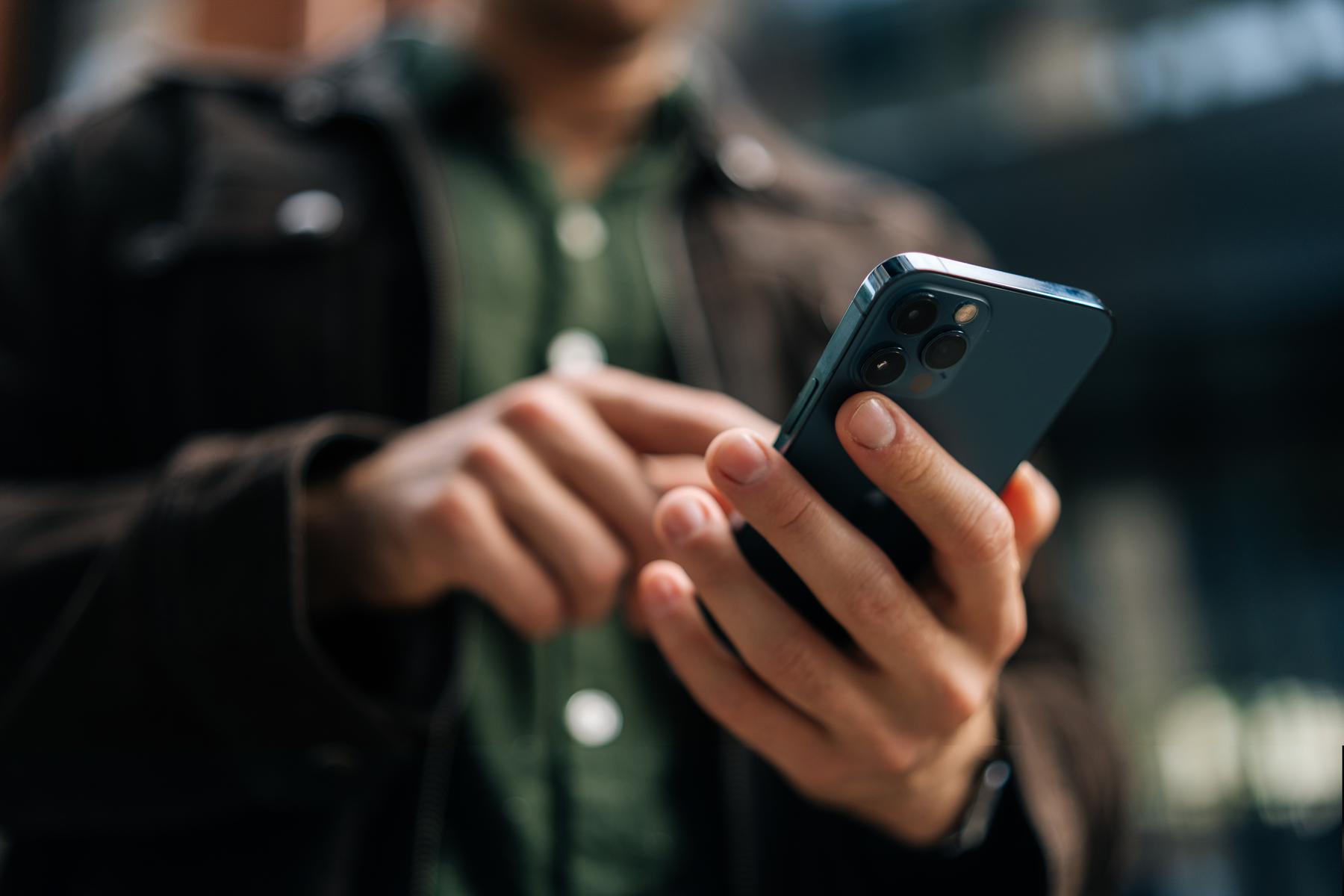 Man in blouse kijkt naar zijn smartphone en typt een bericht, passend bij het oplossen van vragen door Van der Velden Adviseurs.