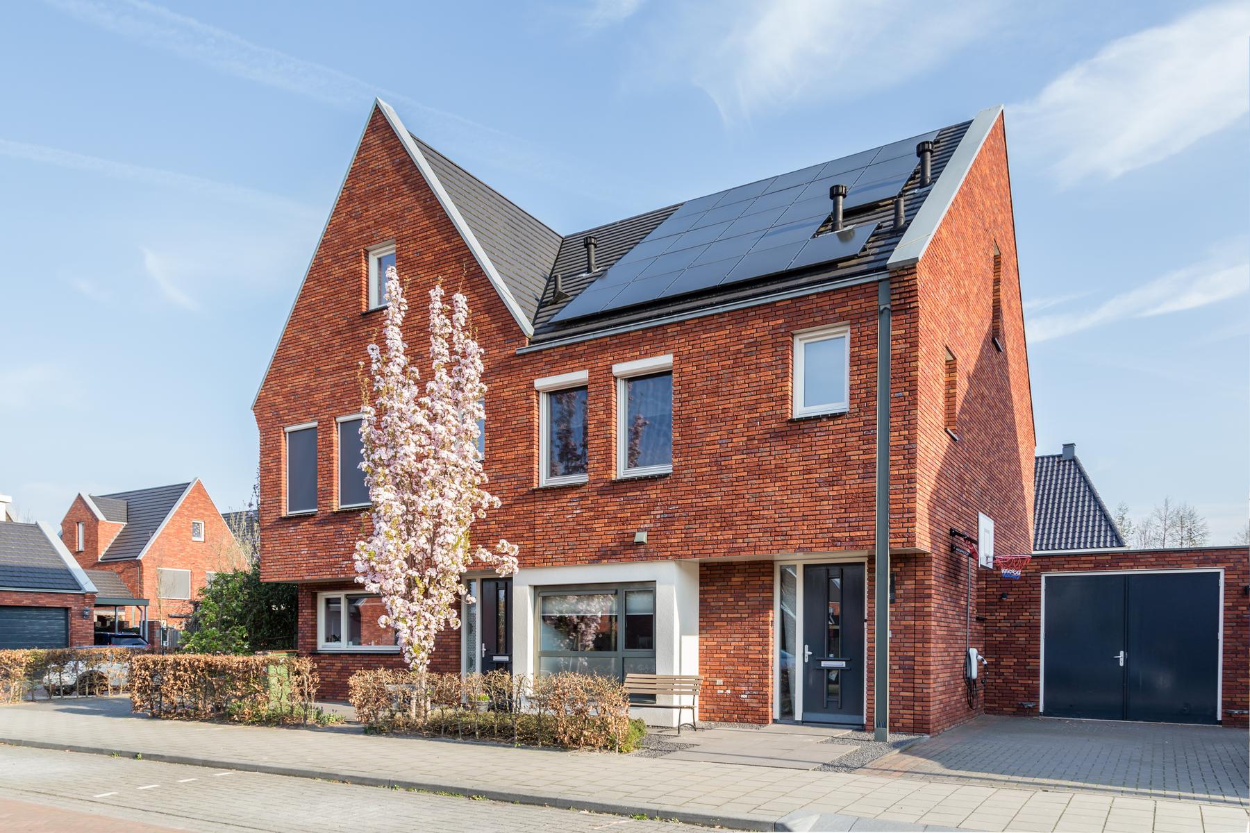 Moderne twee-onder-een-kapwoning met zonnepanelen en bloeiende boom in de voortuin, passend bij de hypotheekrente bekijken.